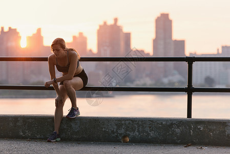 年轻女子在锻炼后坐在水边的栏杆上图片
