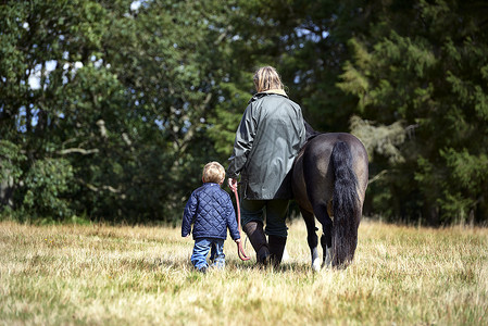逮马的男孩年轻女子带着孩子和小马行走在田间背景