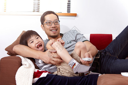 年轻现代中庭由父亲和小儿子组成的现代中庭坐在沙发上家一起看电视图片