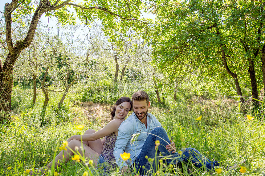 年轻夫妇背对背依靠坐在草地上图片
