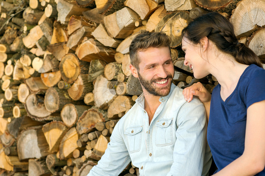 年轻夫妇坐在木堆旁互相对视微笑图片
