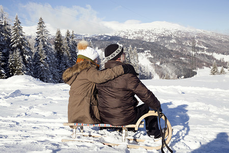 积雪覆盖的山脉上坐在雪橇上眺望远方的夫妇图片