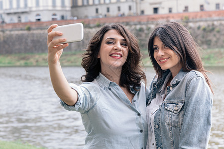 使用智能手机在意大利托斯卡纳佛罗伦萨阿诺河旁自拍的少女们图片