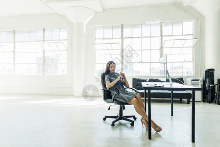 商业妇女靠办公室窗户坐在椅子上图片