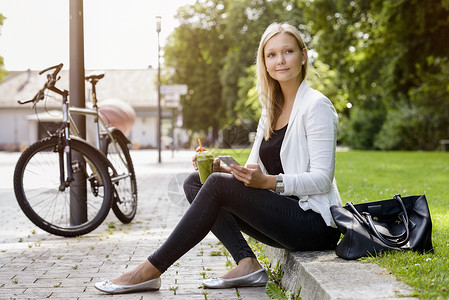 坐在公园台阶上拿着水和智能手机的年轻女子图片