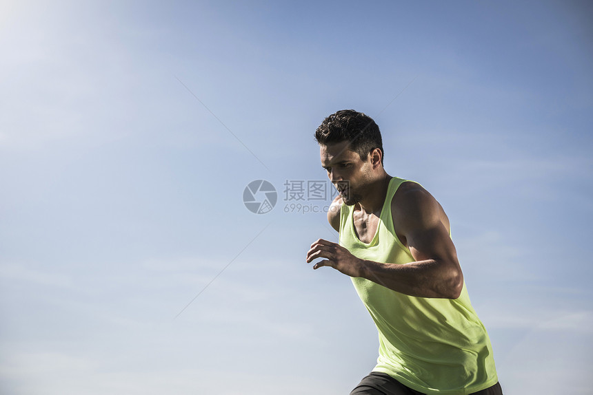 年轻男子穿着背心在蓝天下奔跑图片