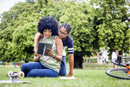 男孩和母亲在公园一起阅读平板电脑图片