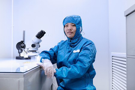 在灵活电子设备工厂清洁室使用显微镜对女工进行肖像图片