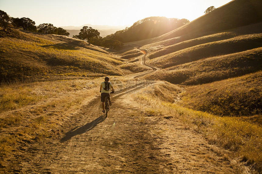 美国加利福尼亚州海湾地区山上年轻人在土路上山地自行车的后视图图片