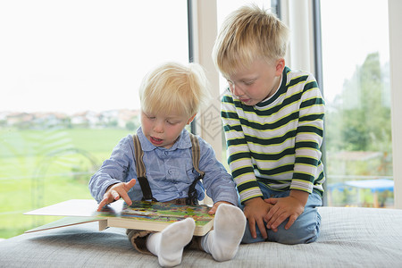 男孩和兄弟在沙发上阅读儿童书图片