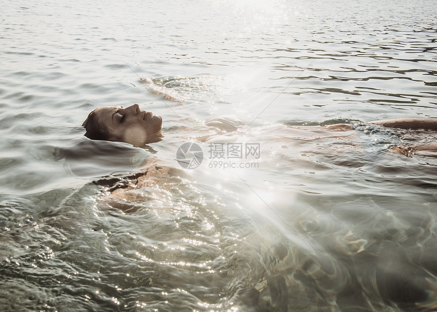 美丽的年轻女子漂浮在阳光明媚的海中图片