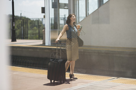 年中成妇女在火车站等候手持轮式提箱和咖啡杯图片