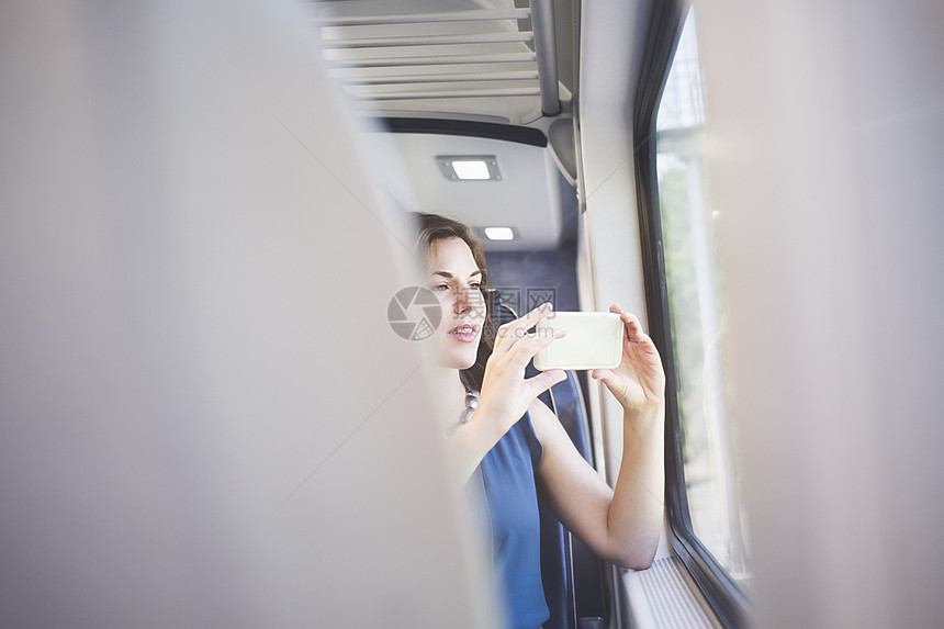 成人中年妇女在火车上用智能手机在窗户上拍照图片