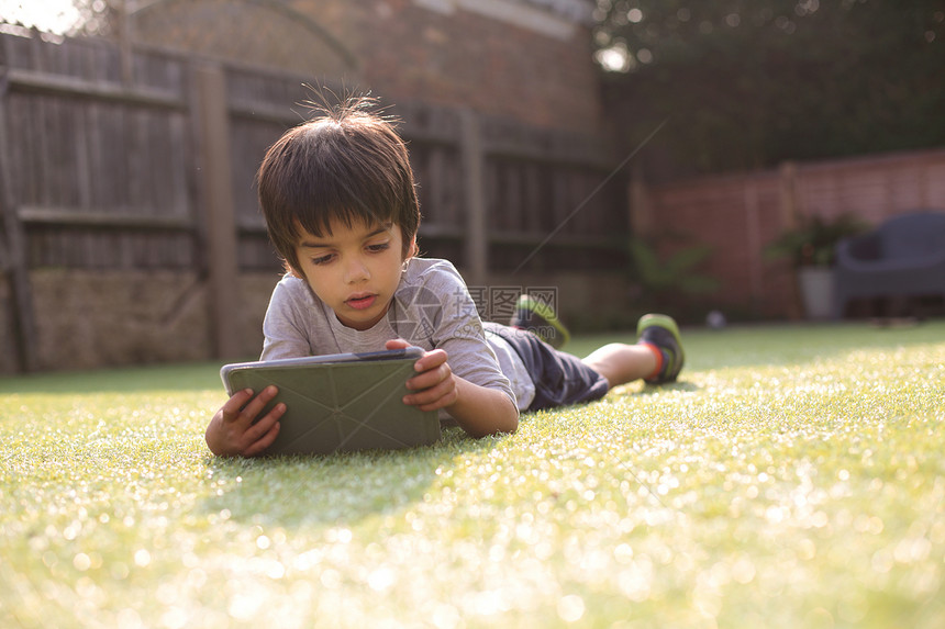 趴在草地上玩平板电脑的男孩图片