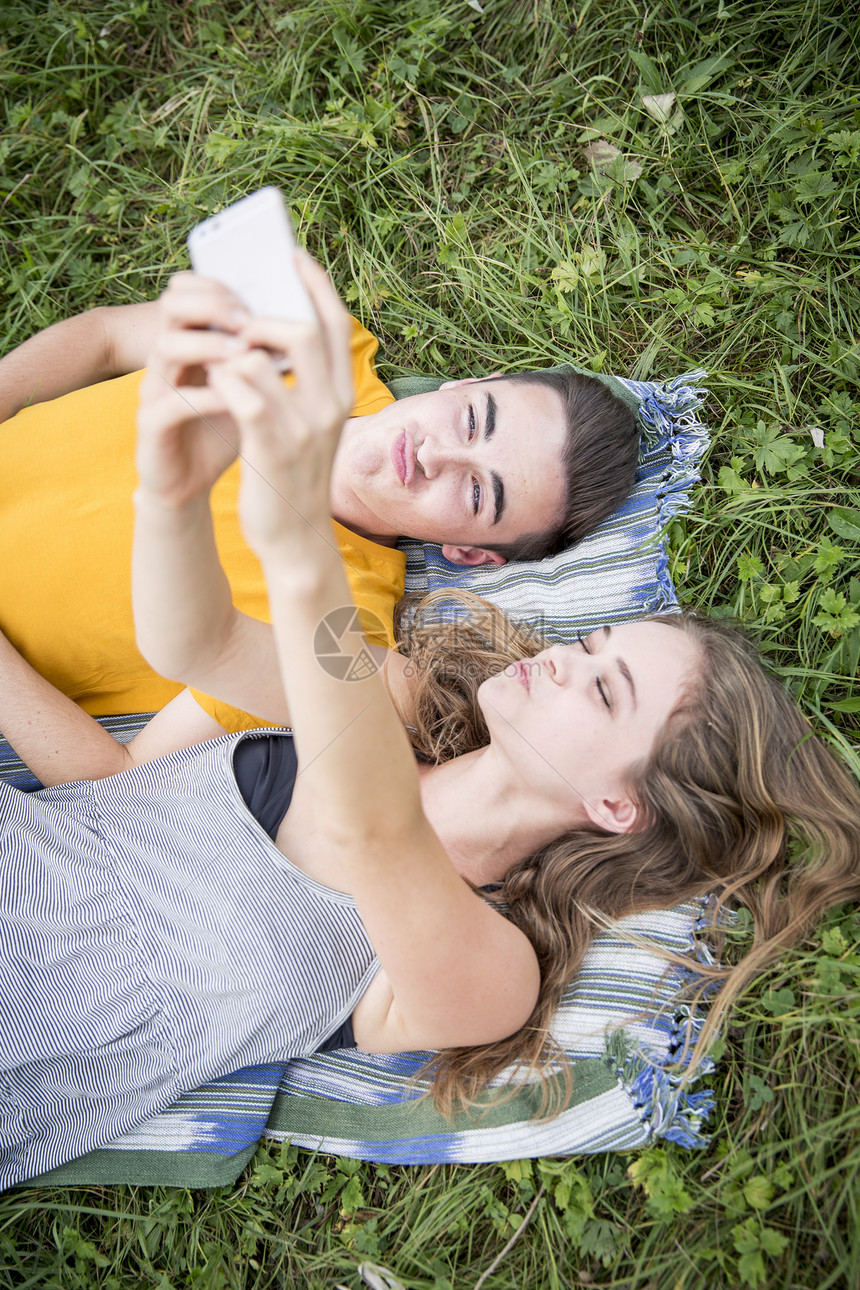 躺在草地上的年轻夫妇使用手机自拍图片