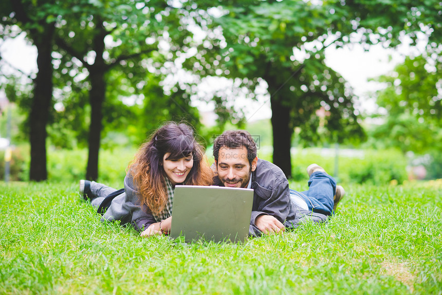 躺在草坪上使用笔记本电脑的情侣图片