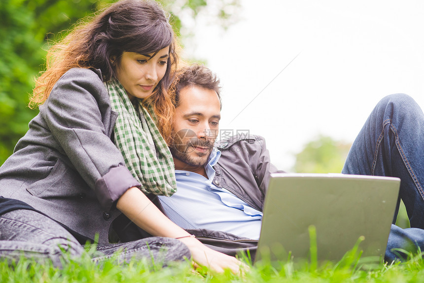 坐在草坪上使用笔记本的情侣图片