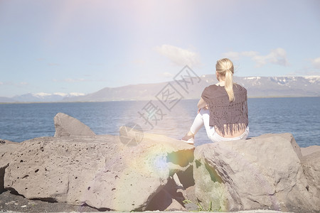 一个女孩坐在海边岩石上俯瞰的后视图图片