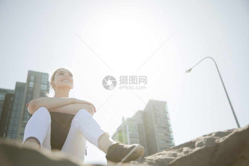 背朝高楼大厦坐在岩石上微笑的少女图片