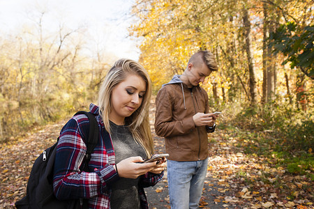 青少年和成年姐妹在秋季森林阅读智能手机短信图片