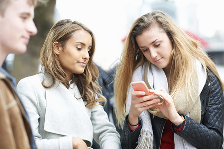 三个朋友在街上阅读智能手机短信图片