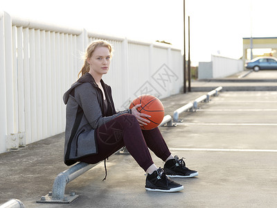 坐在停车场的年轻女篮球运动员背景图片