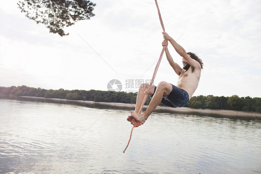 年轻人抓着绳子在湖上摇摆图片