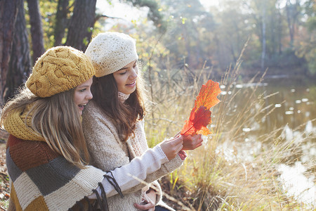 年轻女孩穿着毛衣坐在河边看着秋叶微笑图片