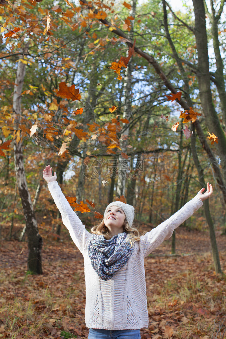 年轻女孩在林中微笑着举起秋叶图片
