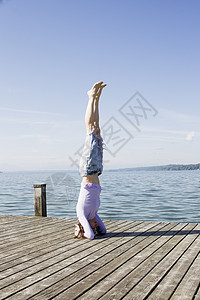 在海边的码头上女人倒立保持瑜伽姿势图片