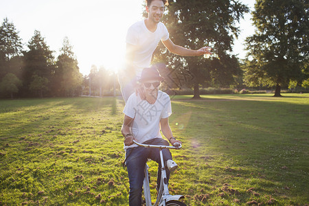 日落时骑自行车后站着去公园的派对男子图片