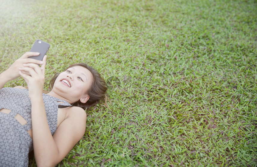 年轻妇女躺在草地上使用智能手机图片