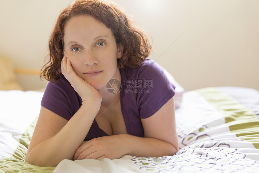 坐在床前的年轻女人手在下巴看着镜头图片