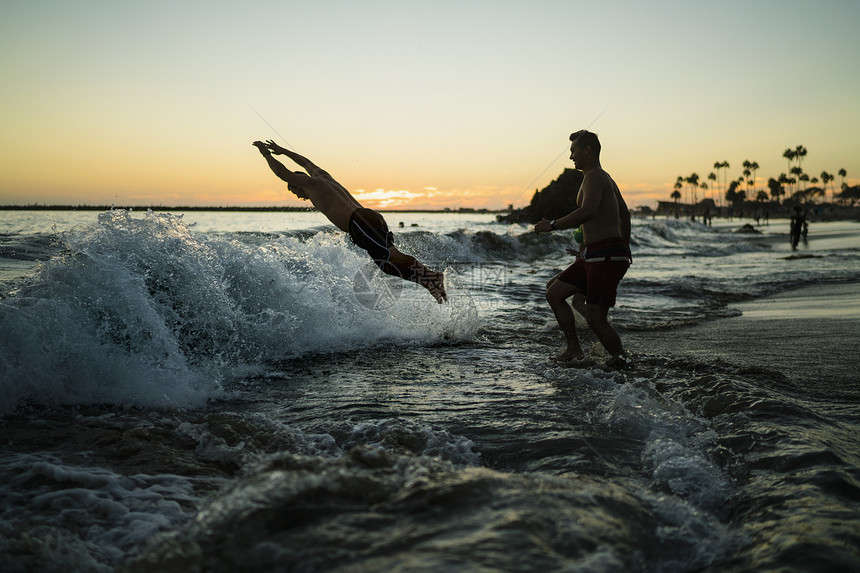 美国加利福尼亚州纽波特海滩日落时年轻人潜入海洋图片