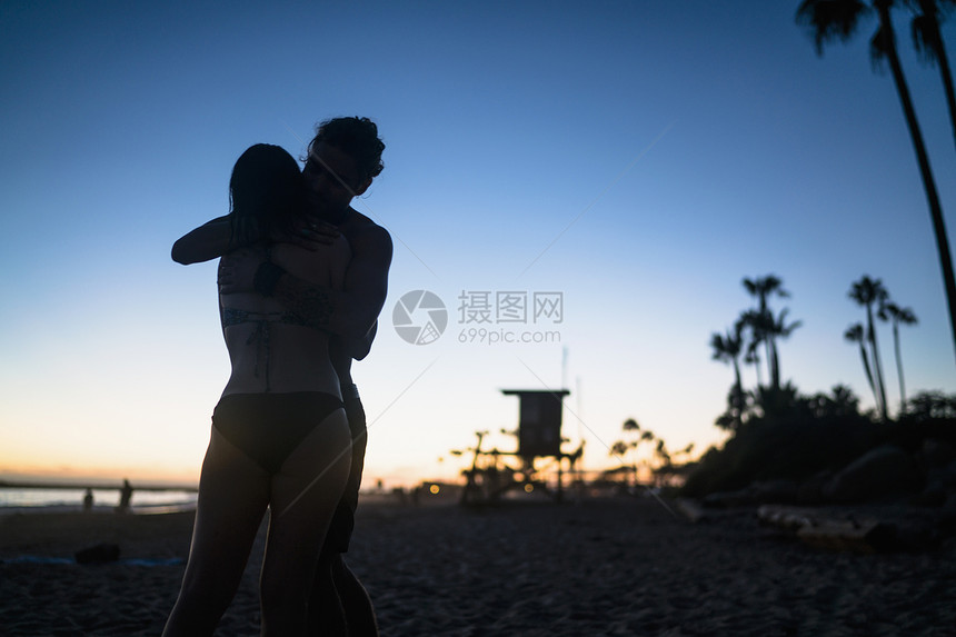 美国加利福尼亚州纽波特海滩日落时拥抱的浪漫年轻夫妇图片