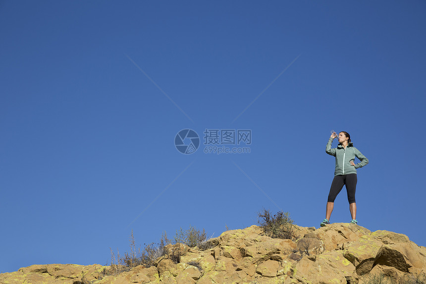 在崎岖的山丘上女跑步者用水瓶喝水图片