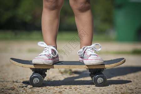 身着帆布鞋的女孩腿站在滑板上图片