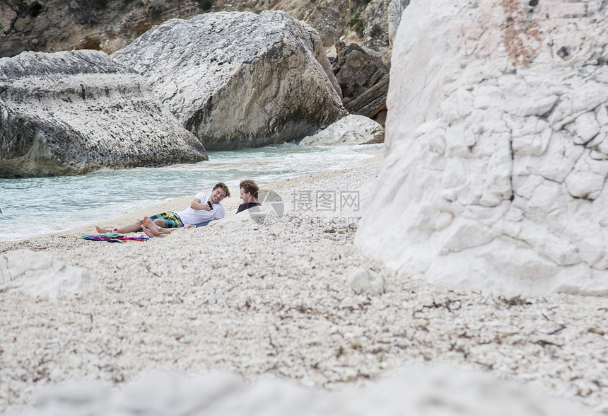 年轻人在岩石海滩上玩手机意大利撒丁岛图片