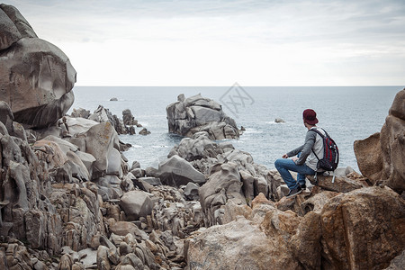 意大利撒丁岛斯梅拉达海岸坐在岩石上看海景的年轻人的背影图片