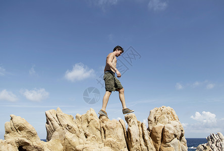 年轻人爬上岩石的低角度视意大利撒丁岛科斯塔帕拉迪索图片