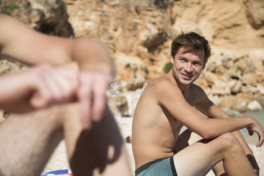 坐在海滩上与朋友微笑的年轻人侧脸图片
