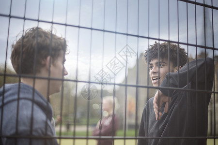 两个男青年靠着栅栏说话图片