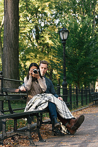 情侣坐在公园长椅上拍照图片