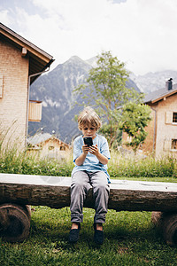 坐在木椅上用数码相机拍摄的男孩背景图片