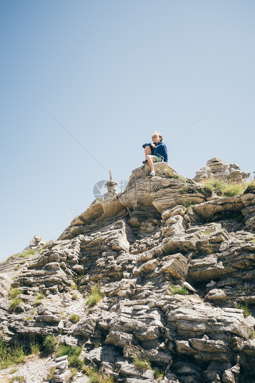 男孩坐在岩石上向远看图片