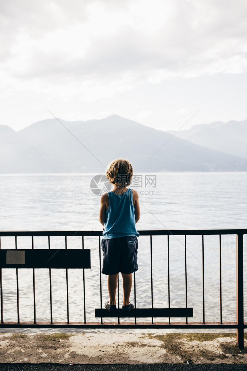 男孩站在栏杆上眺望山脉图片