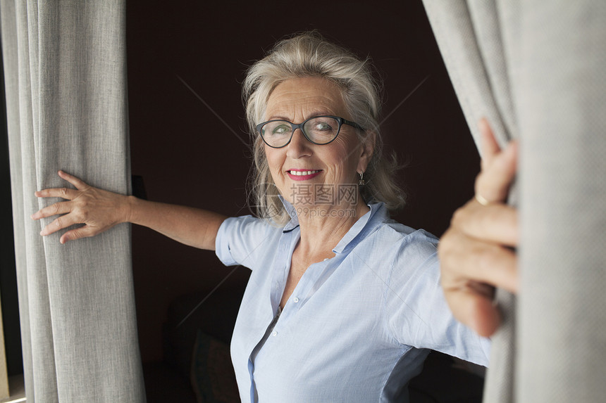 高龄妇女打开窗帘微笑着图片