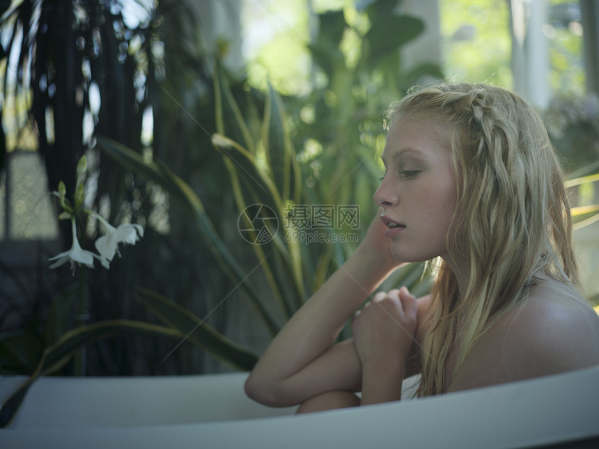 坐在室里满是植物的浴缸里的年轻女人图片
