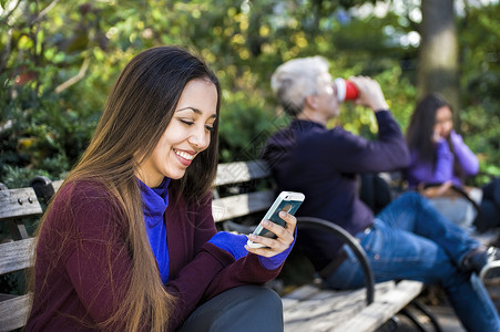 坐在公园长椅上阅读智能手机短信的年轻妇女图片