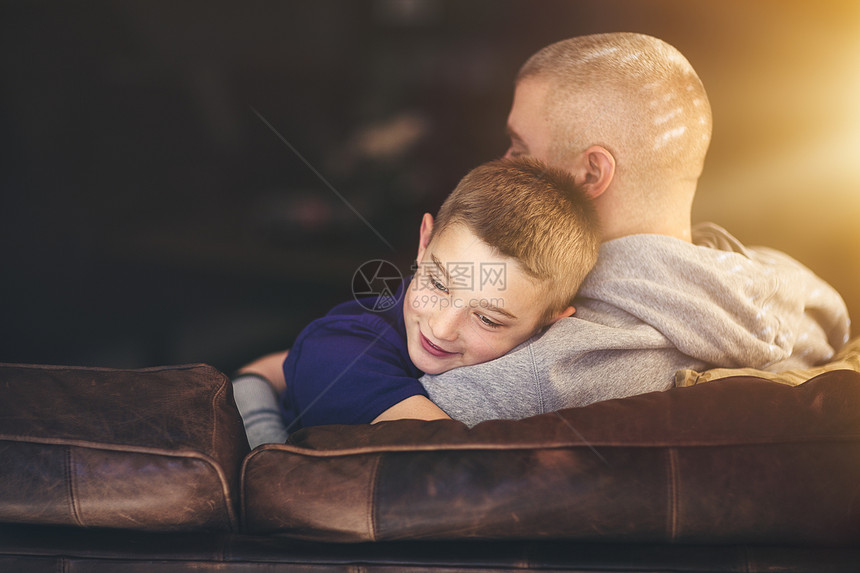 成熟的男子放松在沙发抱儿子图片